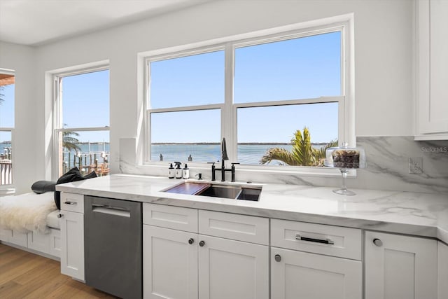 kitchen featuring light wood finished floors, a sink, white cabinets, a water view, and stainless steel dishwasher