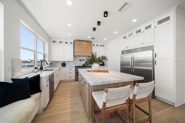 kitchen with visible vents, a sink, high quality appliances, tasteful backsplash, and a center island