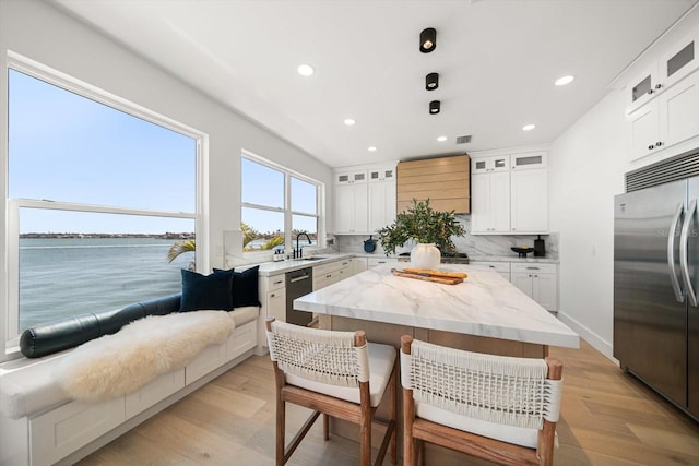 kitchen featuring light stone countertops, a kitchen island, a breakfast bar, light wood-style flooring, and appliances with stainless steel finishes