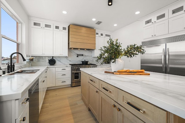 kitchen featuring a sink, premium appliances, light stone counters, tasteful backsplash, and custom exhaust hood