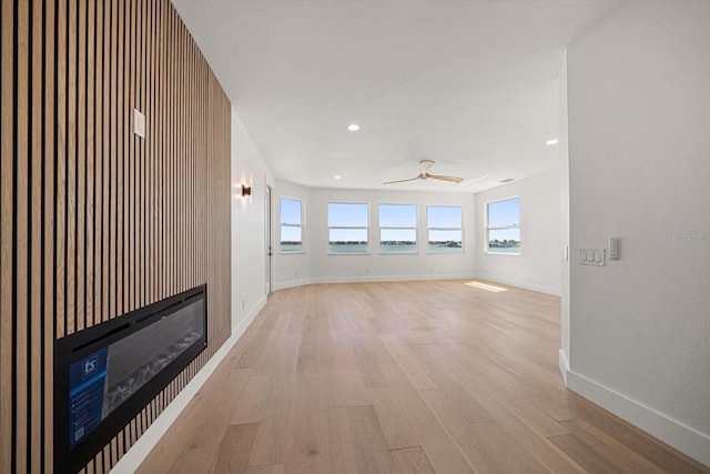 interior space featuring a ceiling fan, a glass covered fireplace, recessed lighting, light wood-style floors, and baseboards