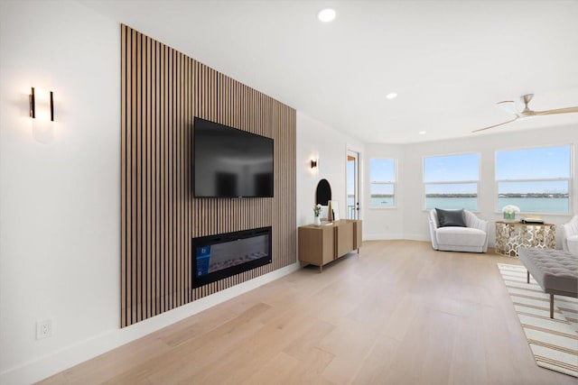 living room featuring baseboards, recessed lighting, light wood-style floors, a glass covered fireplace, and a ceiling fan