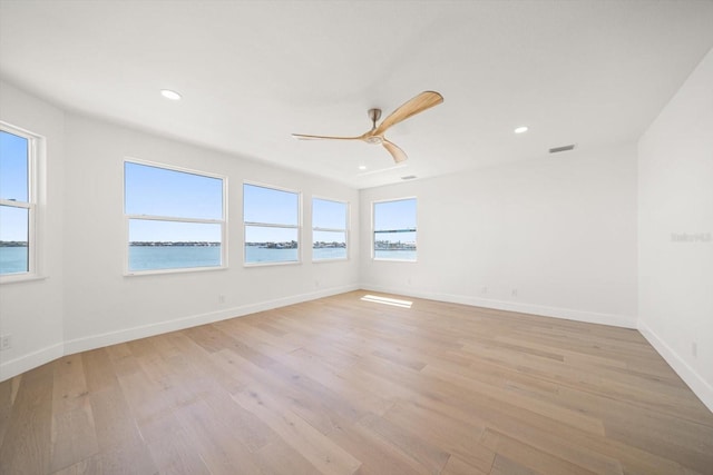 unfurnished room with a ceiling fan, baseboards, light wood-style flooring, recessed lighting, and a water view