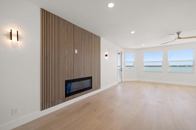 unfurnished living room with a wealth of natural light, baseboards, light wood-style floors, and a glass covered fireplace