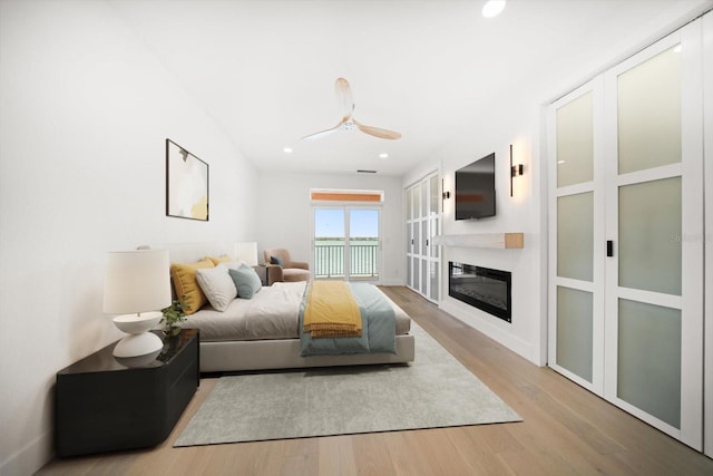 bedroom featuring a glass covered fireplace, a ceiling fan, wood finished floors, and recessed lighting