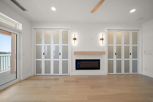 unfurnished living room with visible vents, recessed lighting, light wood-style floors, and a glass covered fireplace