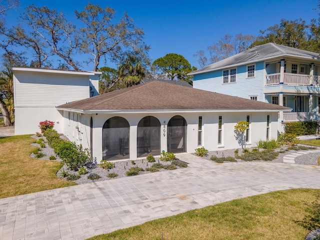 rear view of property with stucco siding, a shingled roof, and a yard