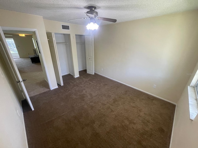 unfurnished bedroom featuring visible vents, two closets, a textured ceiling, dark colored carpet, and baseboards