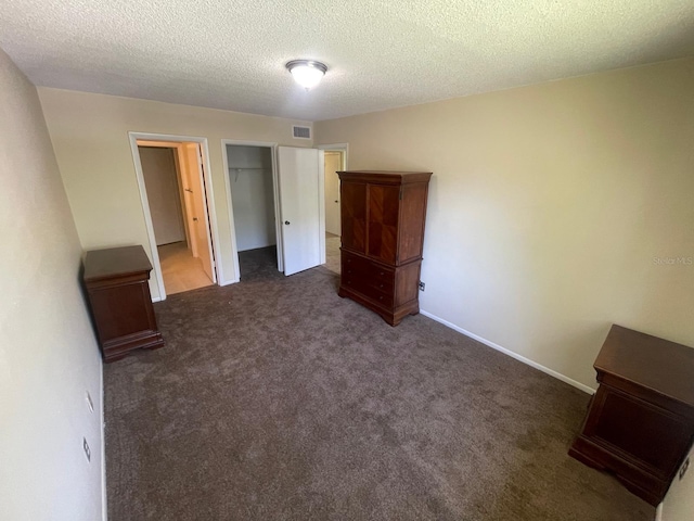 unfurnished bedroom featuring visible vents, baseboards, a closet, a textured ceiling, and dark colored carpet