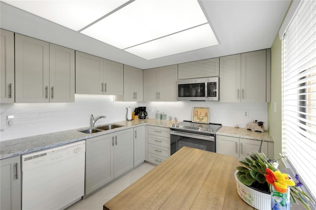 kitchen featuring backsplash, appliances with stainless steel finishes, gray cabinetry, and a sink