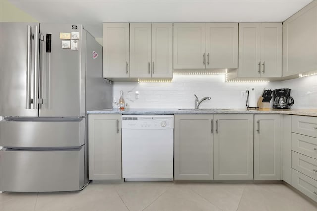 kitchen with a sink, backsplash, freestanding refrigerator, and white dishwasher