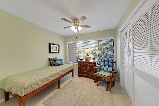 bedroom with ceiling fan, light tile patterned floors, a closet, and a textured ceiling