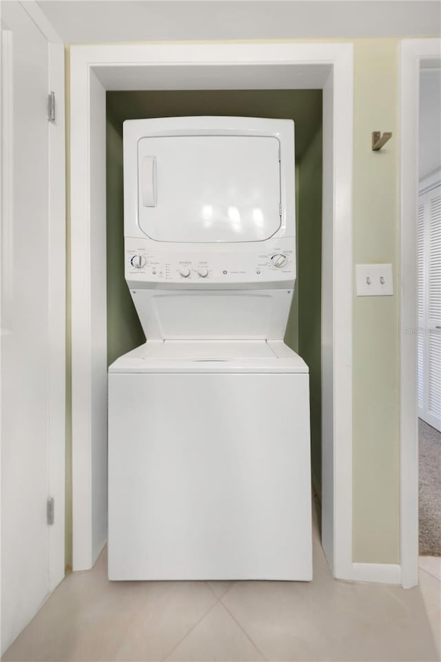 clothes washing area featuring light tile patterned flooring, stacked washer / dryer, and laundry area