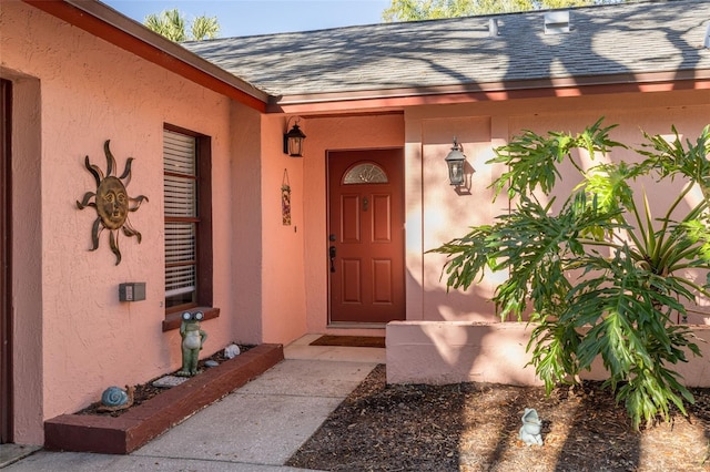 entrance to property featuring stucco siding and a shingled roof