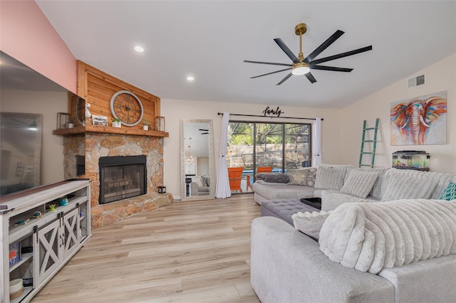 living room with visible vents, lofted ceiling, ceiling fan, a stone fireplace, and light wood-style floors