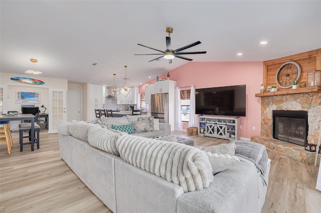 living area with ceiling fan, lofted ceiling, a stone fireplace, recessed lighting, and light wood-style floors