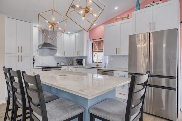 kitchen featuring a sink, appliances with stainless steel finishes, white cabinets, wall chimney range hood, and vaulted ceiling