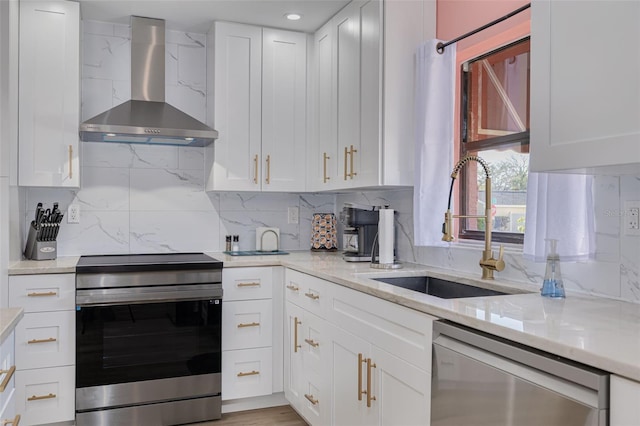 kitchen featuring a sink, decorative backsplash, stainless steel appliances, white cabinetry, and wall chimney range hood