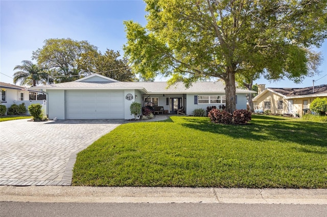 ranch-style home with decorative driveway, a front yard, an attached garage, and stucco siding