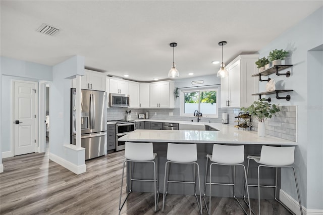 kitchen featuring visible vents, a peninsula, stainless steel appliances, white cabinetry, and a sink