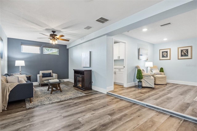 living area featuring visible vents, ceiling fan, baseboards, and wood finished floors