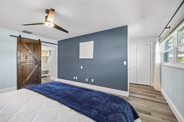 bedroom with visible vents, baseboards, a barn door, and wood finished floors