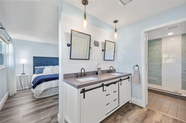 full bath featuring tiled shower, wood finished floors, visible vents, and a sink