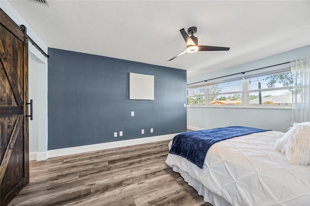 bedroom with baseboards, a barn door, and wood finished floors