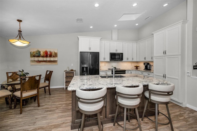 kitchen with visible vents, black microwave, refrigerator with ice dispenser, vaulted ceiling with skylight, and a sink