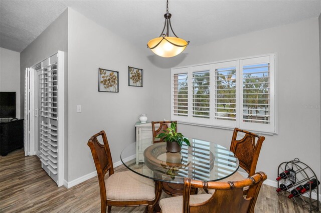 dining space with a textured ceiling, baseboards, and wood finished floors