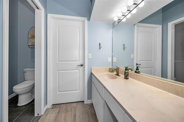 bathroom featuring baseboards, toilet, vanity, wood finished floors, and a textured ceiling