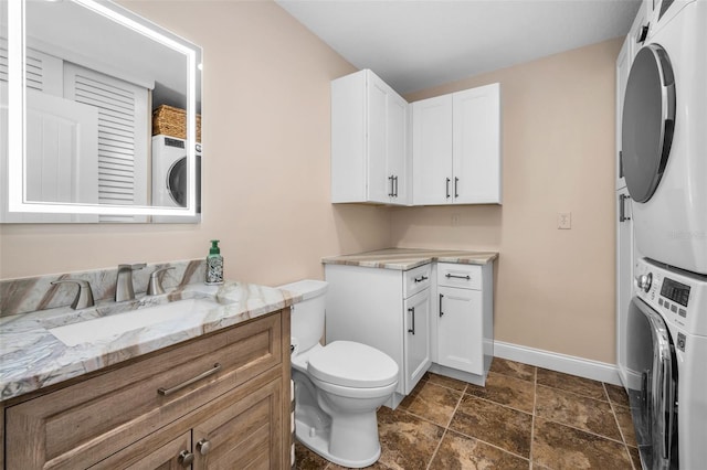 bathroom with baseboards, toilet, stacked washer and clothes dryer, and vanity