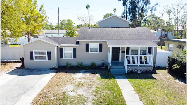 view of front of house with roof with shingles, covered porch, a front yard, and fence