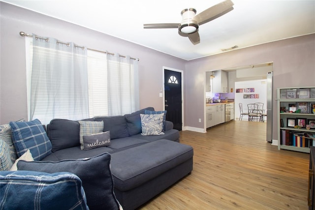 living room with light wood-type flooring, visible vents, baseboards, and ceiling fan