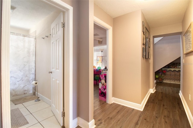 hallway with a textured ceiling, baseboards, and wood finished floors