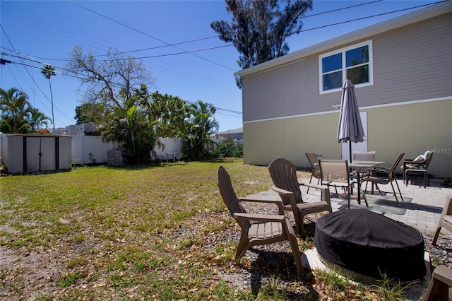 view of yard with fence, an outdoor fire pit, an outdoor structure, a storage shed, and a patio area