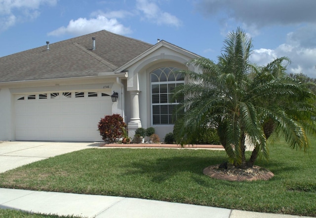 ranch-style house featuring an attached garage, a shingled roof, a front yard, stucco siding, and driveway