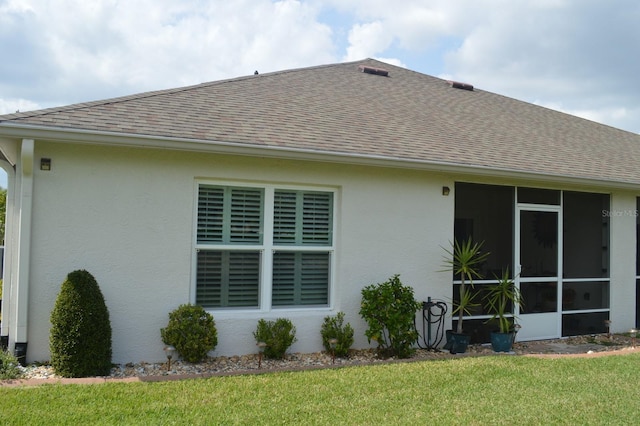 rear view of house with a sunroom, a lawn, roof with shingles, and stucco siding