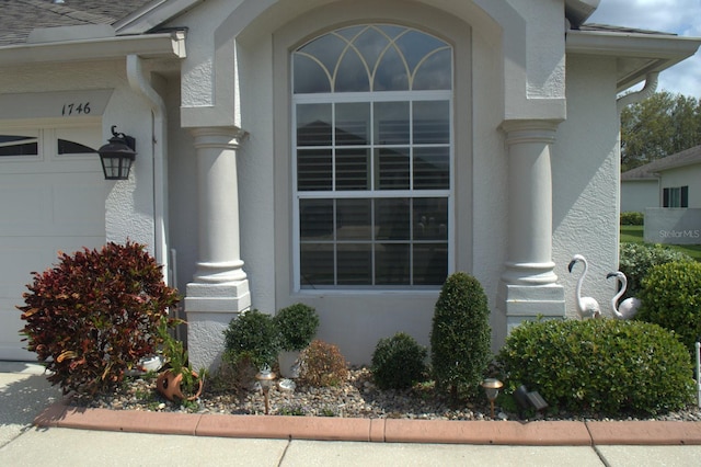 doorway to property featuring an attached garage, roof with shingles, and stucco siding