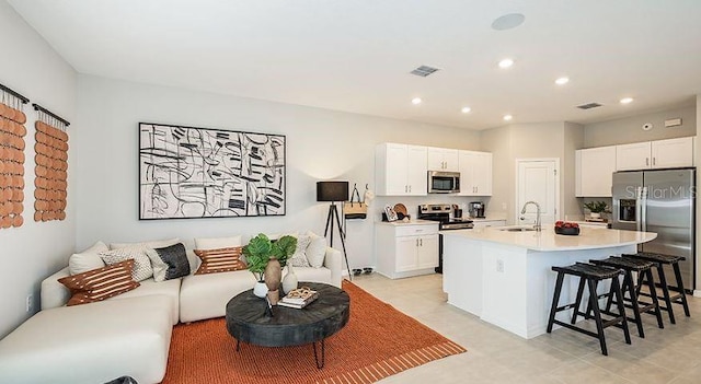 kitchen with an island with sink, a sink, light countertops, appliances with stainless steel finishes, and a kitchen bar