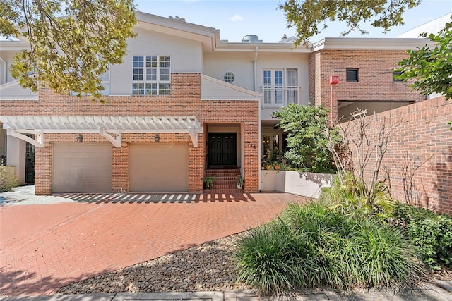 multi unit property with stucco siding, decorative driveway, brick siding, and a garage