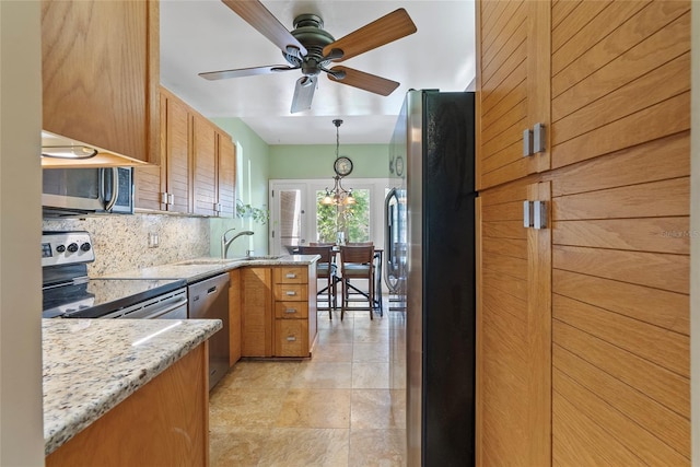 kitchen featuring pendant lighting, ceiling fan with notable chandelier, light stone counters, stainless steel appliances, and decorative backsplash