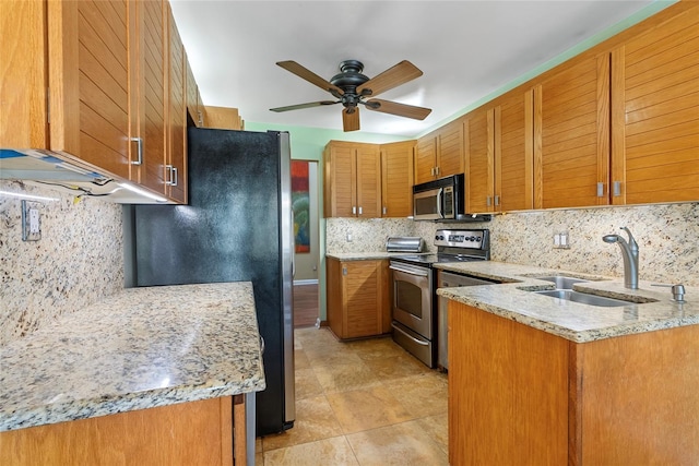 kitchen featuring light stone counters, brown cabinetry, a sink, decorative backsplash, and stainless steel appliances