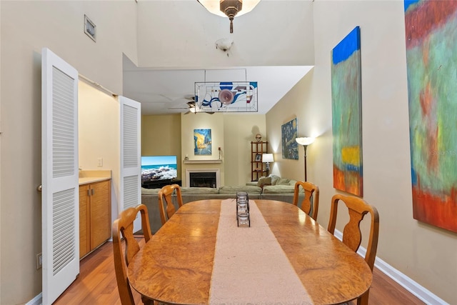 dining space featuring baseboards, a ceiling fan, light wood-style flooring, and a fireplace