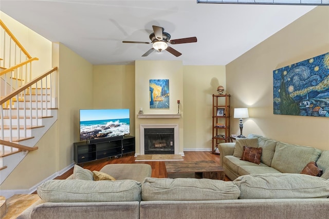 living area with a fireplace with raised hearth, wood finished floors, stairway, baseboards, and ceiling fan