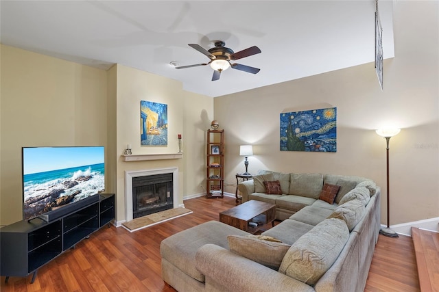 living room featuring ceiling fan, wood finished floors, baseboards, and a fireplace with raised hearth