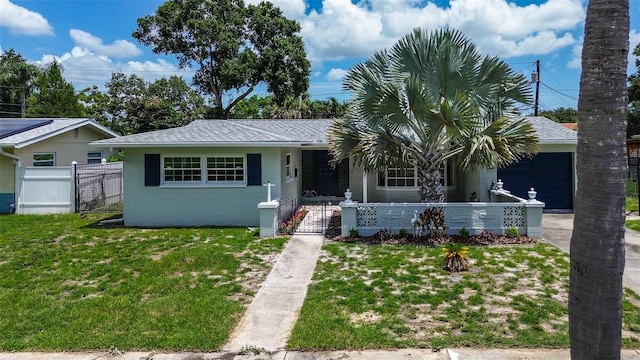 ranch-style house featuring concrete block siding, a front yard, roof with shingles, a garage, and a fenced front yard