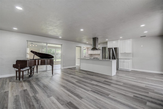 kitchen with island exhaust hood, freestanding refrigerator, wood finished floors, a textured ceiling, and white cabinetry