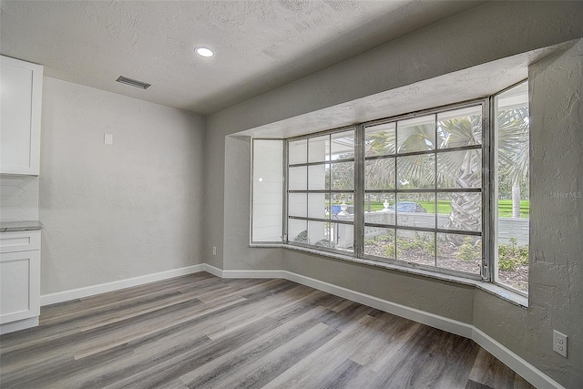 unfurnished dining area with visible vents, a textured ceiling, light wood-type flooring, and baseboards