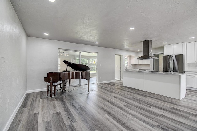 kitchen featuring island exhaust hood, wood finished floors, freestanding refrigerator, white cabinets, and a textured wall